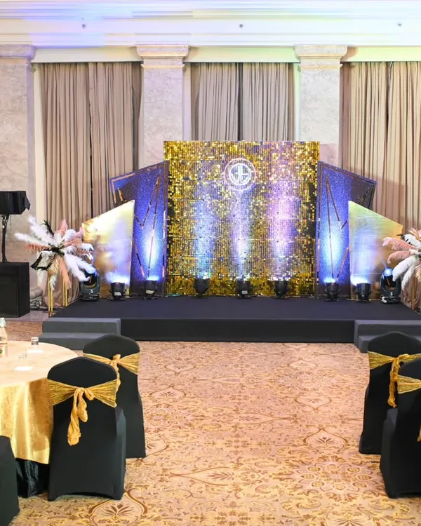 The main ballroom setup for a Great Gatsby themed corporate party. The stage, with its glittering gold backdrop and art deco wings, was the centerpiece, complemented by themed table settings for a cohesive look.