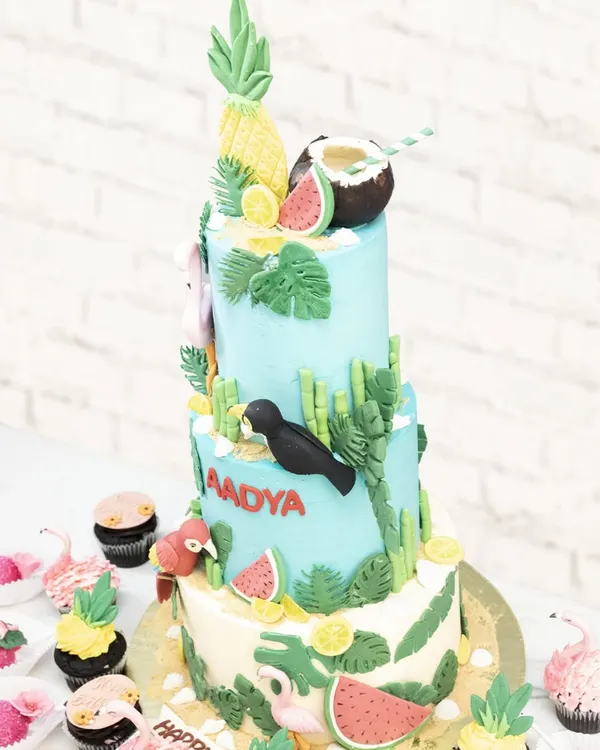 A full view of the three-tiered tropical adventure cake, surrounded by matching flamingo and pineapple cupcakes.