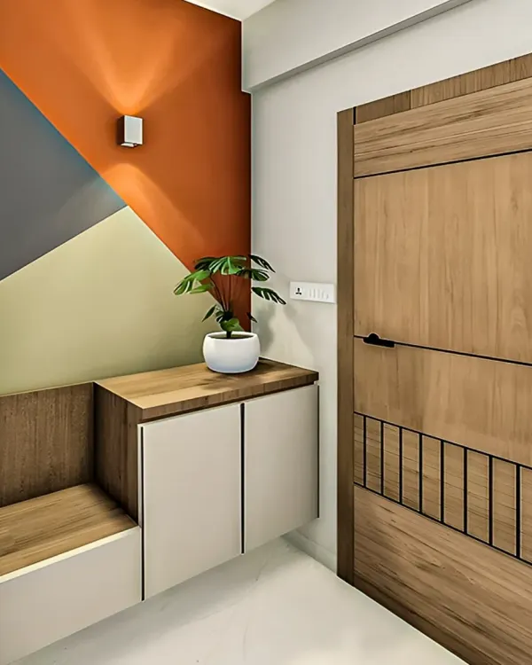 A modern entryway featuring a geometric color-block accent wall. The space includes a floating cabinet and a built-in wooden bench, combining bold design with practical function.