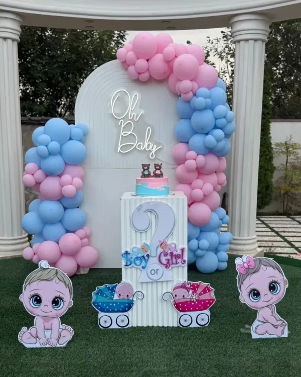 A complete gender reveal party setup with an "Oh Baby" neon sign. This outdoor decoration includes a "Boy or Girl?" pedestal, cute baby cutouts, and a pink and blue balloon arch against a white backdrop.