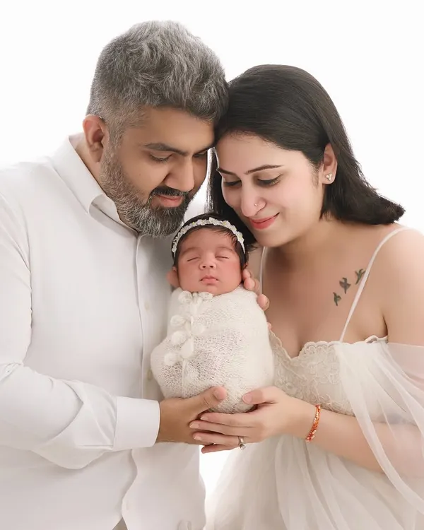 A beautiful family portrait where both parents gaze lovingly at their swaddled newborn, creating a classic and timeless memory in our all-white studio setup.