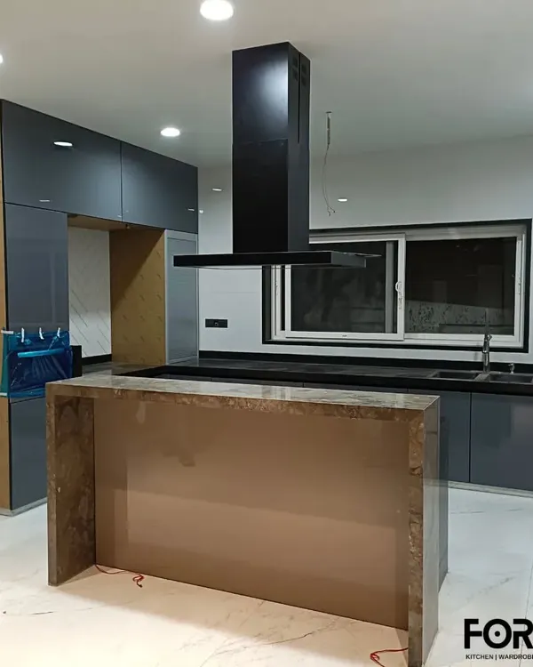 A luxurious open-plan kitchen with a large central island and an integrated chimney. The dark grey back-painted glass cabinets and marble-finish island create a dramatic and sophisticated focal point in the home.