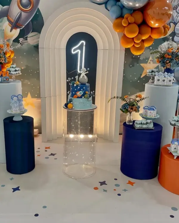 Our space-themed parties are an adventure for the imagination. This setup for a first birthday includes a galaxy backdrop, a rocket ship, planet-themed desserts, and a glowing number '1'.