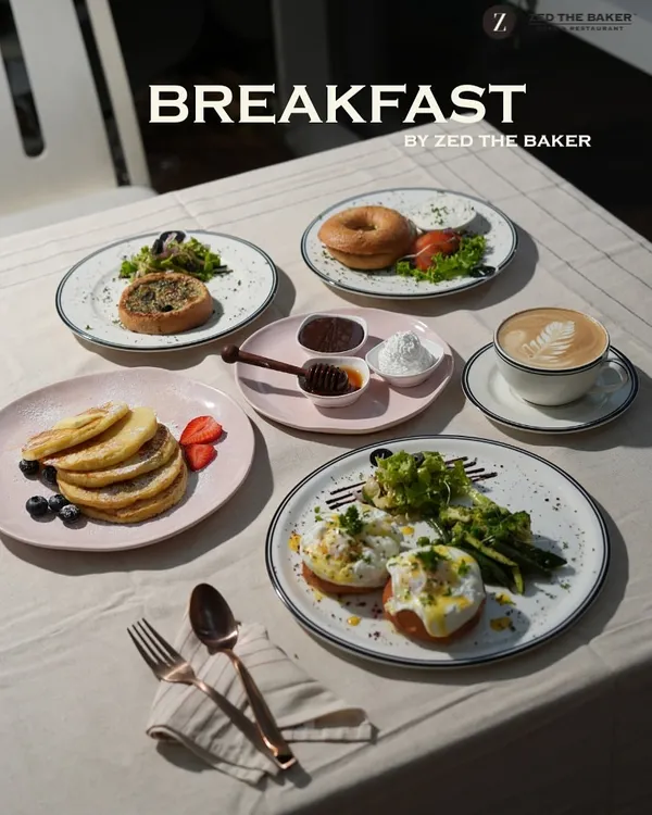 A glimpse of the perfect breakfast spread. It features fluffy pancakes with fresh berries, classic eggs benedict, a savory bagel, and a freshly brewed cappuccino to start your day right.