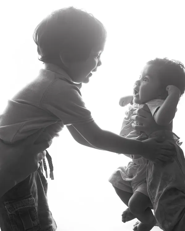 A black and white version of this sweet sibling interaction. The monochrome edit adds a timeless, classic feel to the moment, focusing on the expressions and the connection between them.