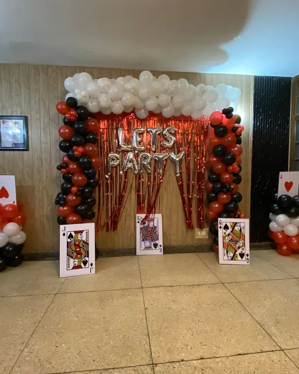 I can create fun, themed party setups like this casino or card party decoration. This design includes balloon pillars, a red tinsel curtain backdrop, 'LET'S PARTY' foil balloons, and large playing card props to complete the look.