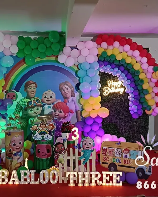 A full-scale Cocomelon themed birthday party. This vibrant setup includes a rainbow balloon arch, character cutouts, a themed backdrop, and even a yellow school bus prop for a completely immersive experience.
