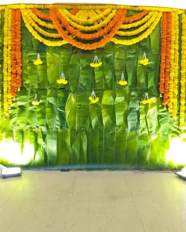 A classic Haldi setup with a backdrop made entirely of fresh banana leaves. The top is decorated with bright yellow and orange marigold garlands, creating a traditional and auspicious look.