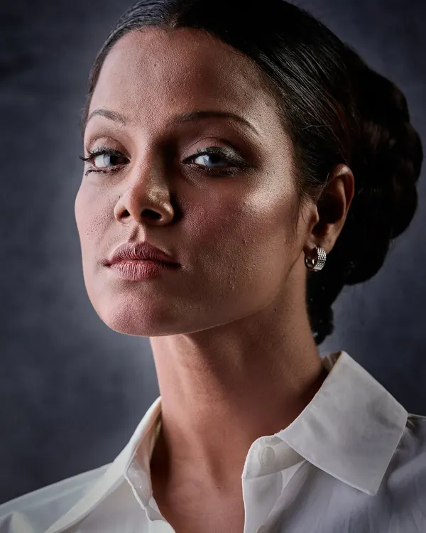 A powerful, high-contrast portrait. In black and white, the focus is on the sculpted features, the intense gaze, and the clean, classic updo. The makeup is designed to define and shape, even without color.