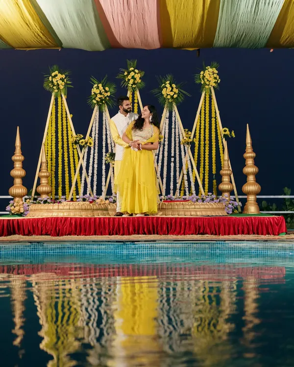 A stunning Haldi portrait by the pool at night. The reflection in the water and the beautifully lit decor create a magical and romantic atmosphere for the couple.