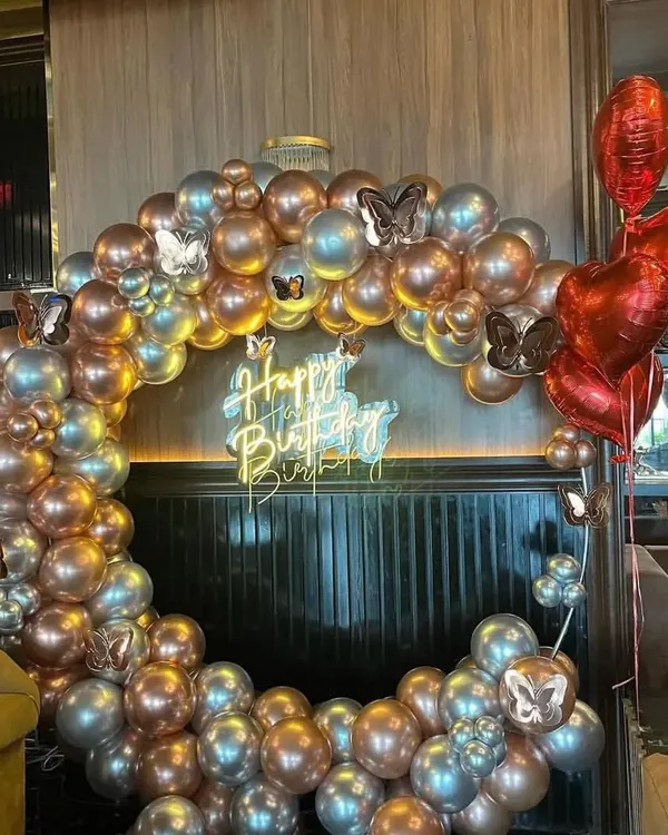 This elegant ring backdrop is made with metallic chrome balloons in silver and rose gold, accented with butterfly details. The neon "Happy Birthday" sign adds a modern touch.