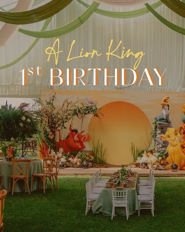 A wide shot of a Lion King first birthday celebration set up in a large outdoor tent. The design features a fully realized Pride Rock backdrop, themed table settings on the lawn, and dramatic fabric draping on the ceiling to mimic the sky.