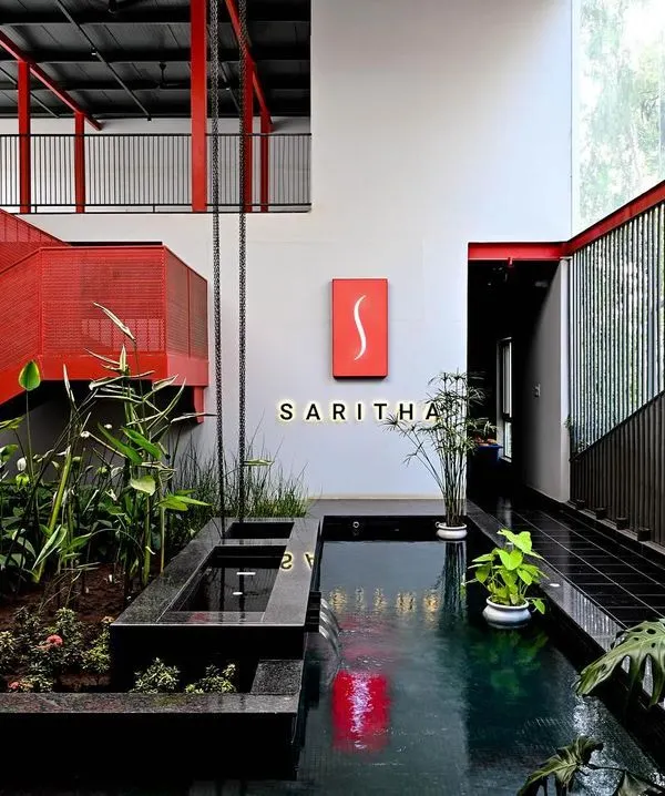 The central atrium of the SARITHA SERENE marketing office is a vibrant and dynamic space. We used a bold red for the structural steel elements, contrasting with the tranquility of the indoor water body and lush planters to create a memorable first impression.