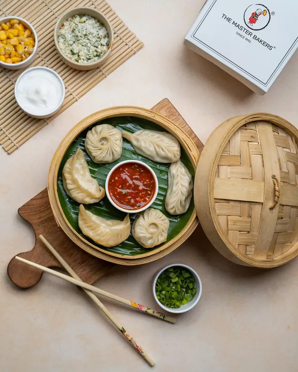 An assortment of our handcrafted momos, featuring both classic pleated and round shapes, served in a traditional bamboo steamer. This platter shows the variety of fillings and styles we offer.