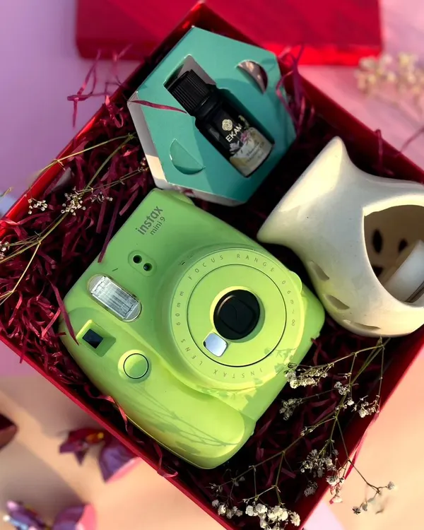 A perfect Valentine's gift for creating memories. This hamper features a bright green Instax Mini camera, an essential oil diffuser, and fragrant diffuser oil, all nestled in a vibrant red gift box.