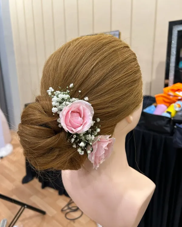 A classic and romantic bridal updo. This beautifully structured bun is adorned with delicate pink roses and baby's breath, perfect for a wedding or reception.