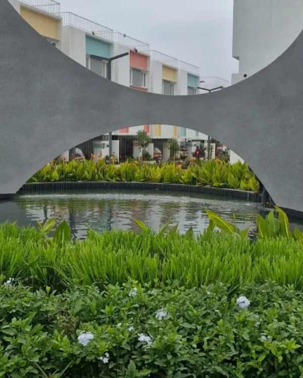 The water and concrete sculpture seen during the day. The strong, curved forms of the concrete contrast with the soft texture of the surrounding aquatic plants, creating a balanced and visually engaging composition.