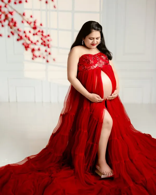 A bold and beautiful portrait in a stunning red tulle gown. The open-front design tastefully showcases the baby bump, celebrating the beauty of the pregnant form.