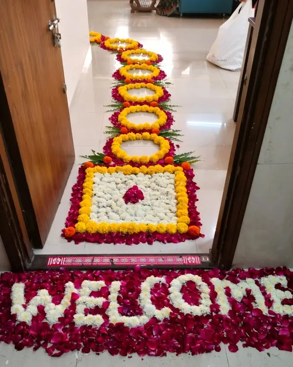A welcoming floral carpet for a home entrance. This design features a pathway of marigold and rose petal rangoli, leading to a "WELCOME" message written entirely with fresh white and red rose petals.