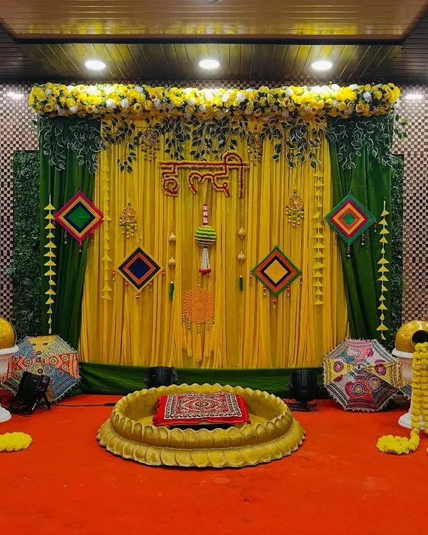 A beautiful Haldi setup with a yellow and green theme, featuring a large lotus-shaped bowl for the ceremony, marigold garlands, and traditional Rajasthani umbrellas.