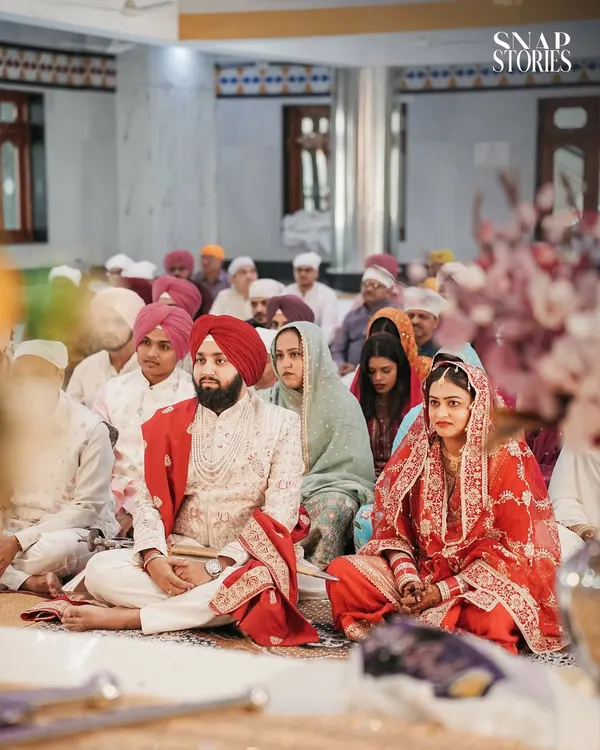 A wide shot of the couple during the Anand Karaj ceremony, surrounded by their family and friends in the Gurudwara. We capture the community and spiritual atmosphere of a Sikh wedding.
