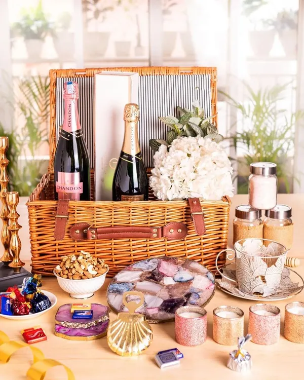 This is the ultimate luxury wedding hamper, overflowing with treats for the new couple. It includes two bottles of champagne, agate coasters, candles, gourmet snacks, and decorative items, all packed in a classic wicker basket.