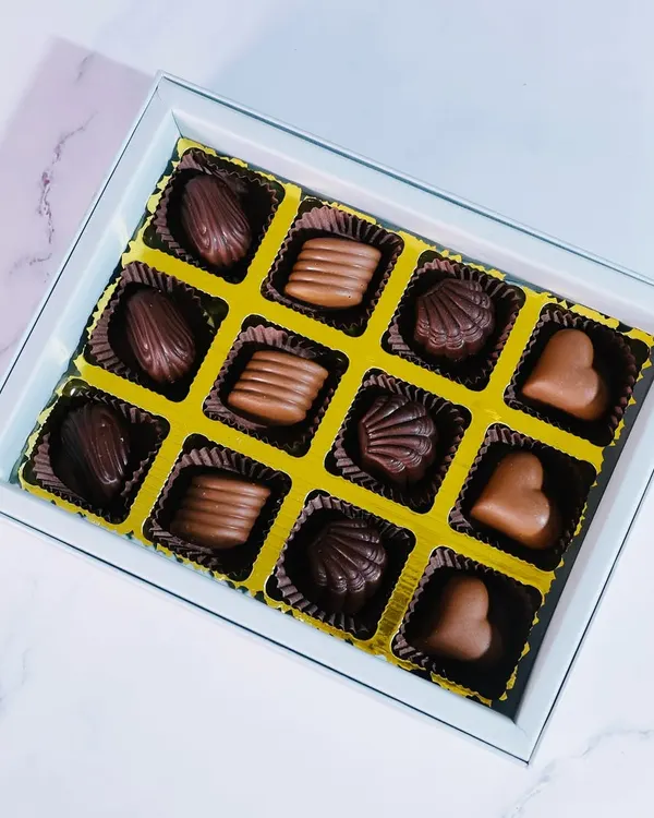A top-down view of my 12-piece praline collection, showcasing the variety of shapes and flavors. You can see heart-shaped milk chocolates, shell-shaped dark chocolates, and more.