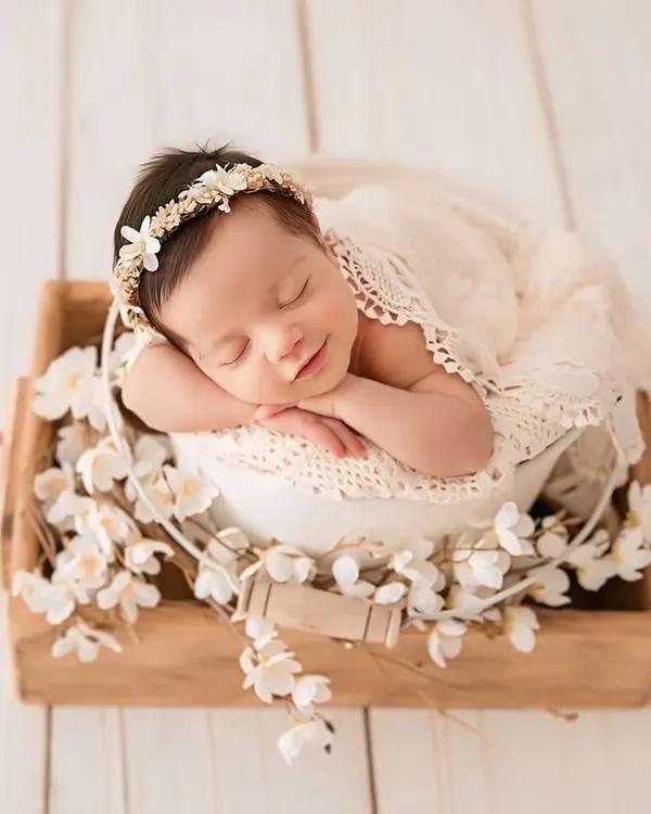 A perfect example of a classic newborn portrait. The baby is posed safely in a white bucket, surrounded by delicate flowers, with a gentle smile that melts your heart. This style is truly timeless.