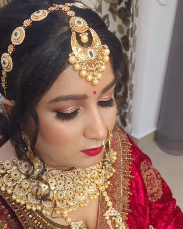 A close-up of a stunning Rajputana bridal look. The focus is on the elaborate matha patti, the classic red lip, and the shimmering eye makeup that defines this royal style.