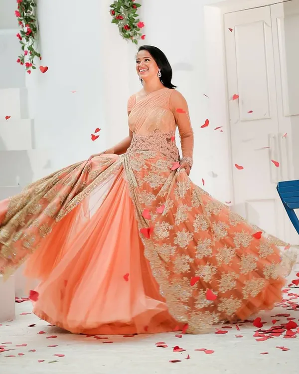 A happy client twirls in a flowing peach gown by Shantanu & Nikhil, perfect for a pre-wedding shoot or reception party. This designer rental gown features delicate lacework over a lightweight tulle skirt.