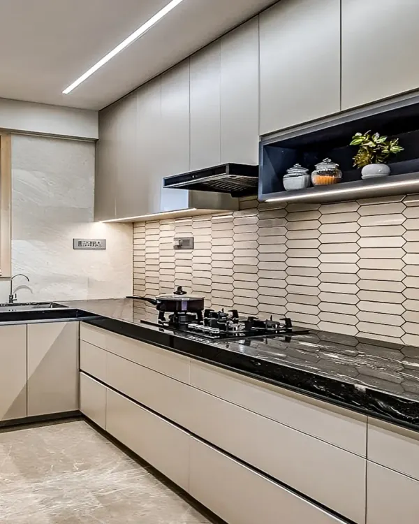 A sleek, contemporary kitchen with handleless cabinets and a black granite countertop. The design includes a unique hexagonal tile backsplash and under-cabinet lighting for a bright and efficient workspace.