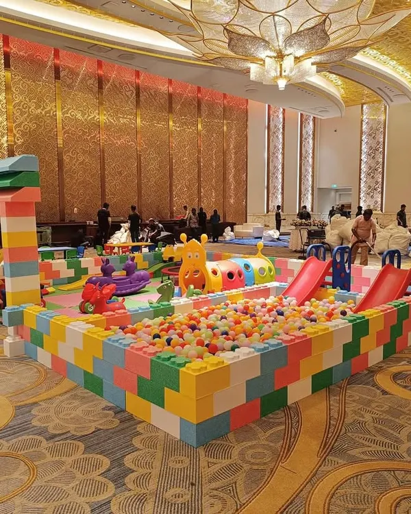 This is our expansive Lego Land Play Area, set up for a large event in a banquet hall. It features a secure enclosure made of giant, colorful blocks, a multi-colored ball pit, dual slides, and various ride-on toys, creating a complete and engaging world for toddlers and young children.