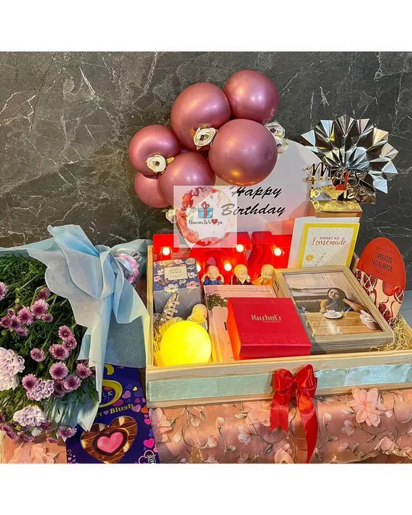 An elaborate birthday tray hamper featuring a pink balloon arrangement, a bouquet of fresh flowers, and a curated selection of gifts including a framed photo and other personal touches.