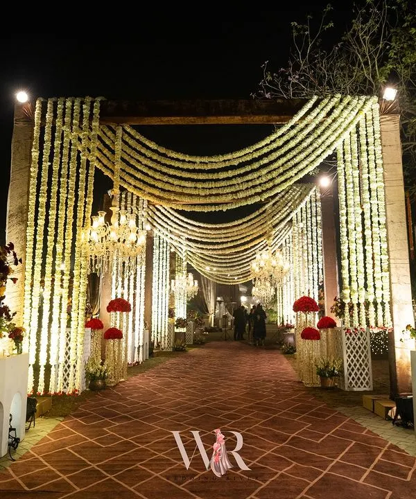 We designed this breathtaking entrance to blend rustic charm with traditional magic. A carpeted walkway is flanked by pillars draped in cascading white mogra, with chandeliers adding a regal glow, creating an enchanting prelude to the wedding celebration.