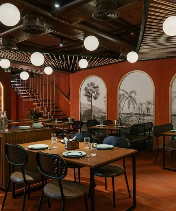 The 'Chambal' restro-bar features an open-plan dining area with a monochromatic red color scheme and rustic brick walls. The design creates a warm, energetic atmosphere perfect for a modern Indian restaurant.