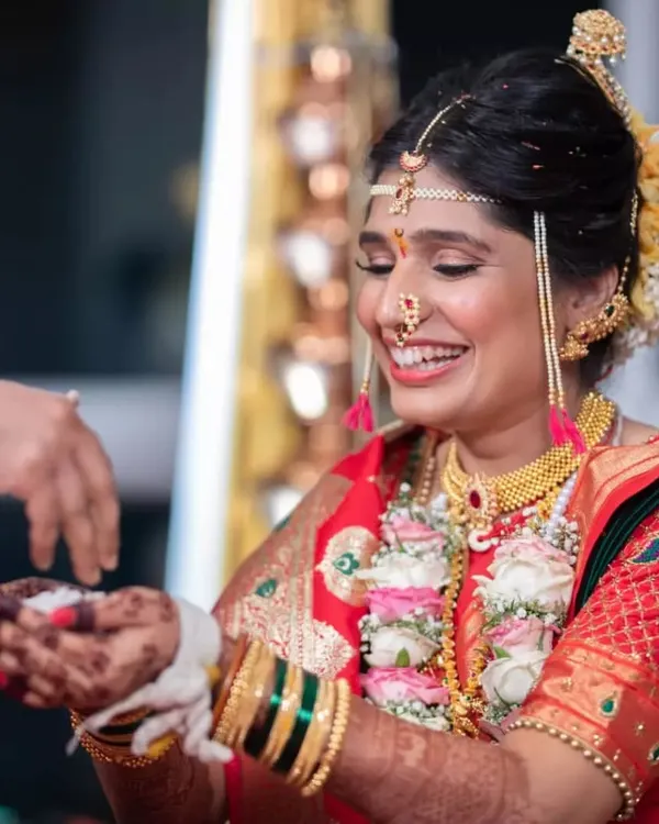 The joy of a Maharashtrian bride during her wedding ceremony. Her radiant smile is the centerpiece, enhanced by a classic makeup look and traditional gold jewelry.