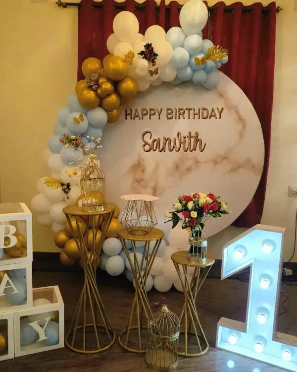 A chic first birthday setup with a blue, white, and gold balloon arch over a marble-print circular backdrop, perfect for a modern celebration.