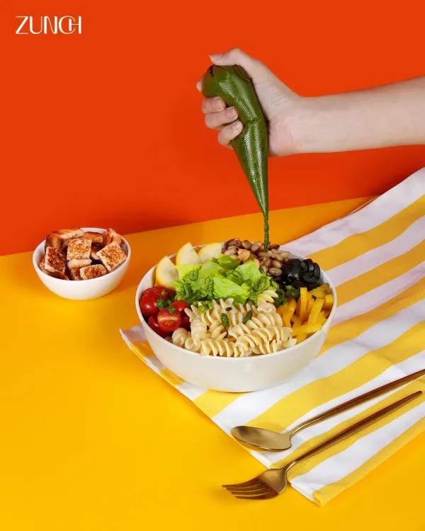 Our Pesto Piccolo bowl getting its final touch. The vibrant pesto dressing brings together pasta, fresh greens, and crunchy toppings for a meal that's bursting with energy.