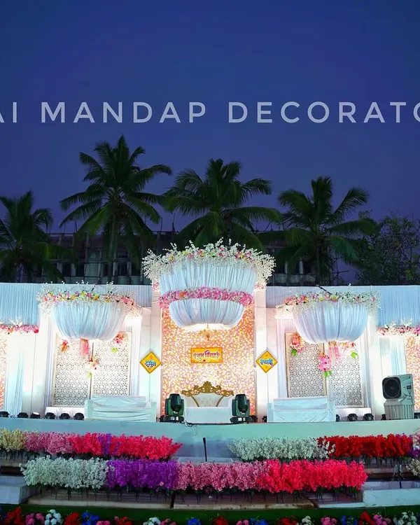 We specialize in creating breathtaking reception stages that leave a lasting impression. This grand outdoor setup features magnificent floral chandeliers, a multi-tiered stage, and beautiful lighting against the evening sky, perfect for a large celebration.