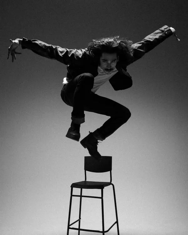 A high-energy, gravity-defying shot of actor Vishak Nair for an editorial. The simple black jacket, white tee, and dark jeans create a classic, rebellious look inspired by rock and roll.
