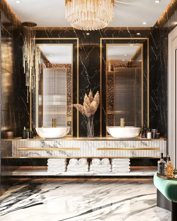 A luxurious bathroom featuring a floating dual-sink vanity set against a black marble wall with gold-framed mirrors. A cascading chandelier and green velvet stool add touches of opulence.