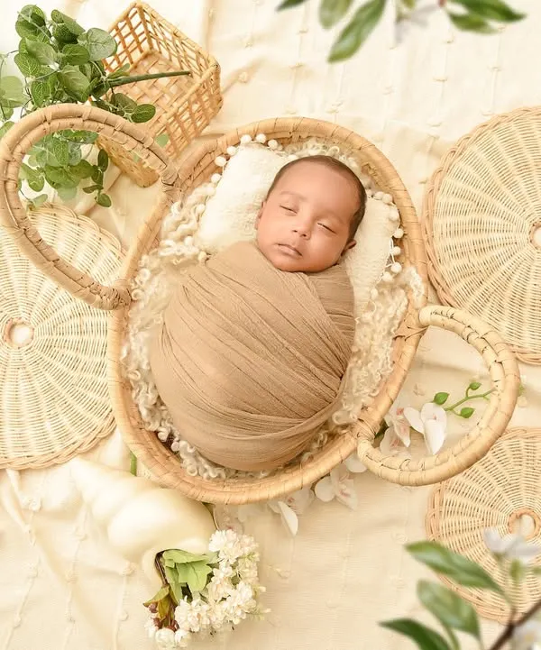 An overhead shot of a newborn in a wicker basket, surrounded by natural textures and greenery. This boho-inspired flat-lay is artistic and beautifully composed.