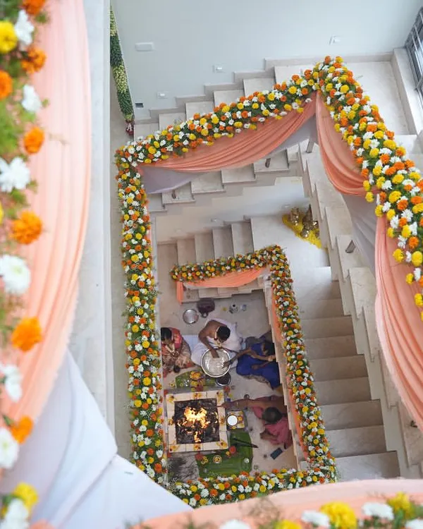 An aerial view of a housewarming ceremony (Griha Pravesh) setup. We created a mandap around the staircase using marigold garlands and drapes, transforming the home's interior for the puja.