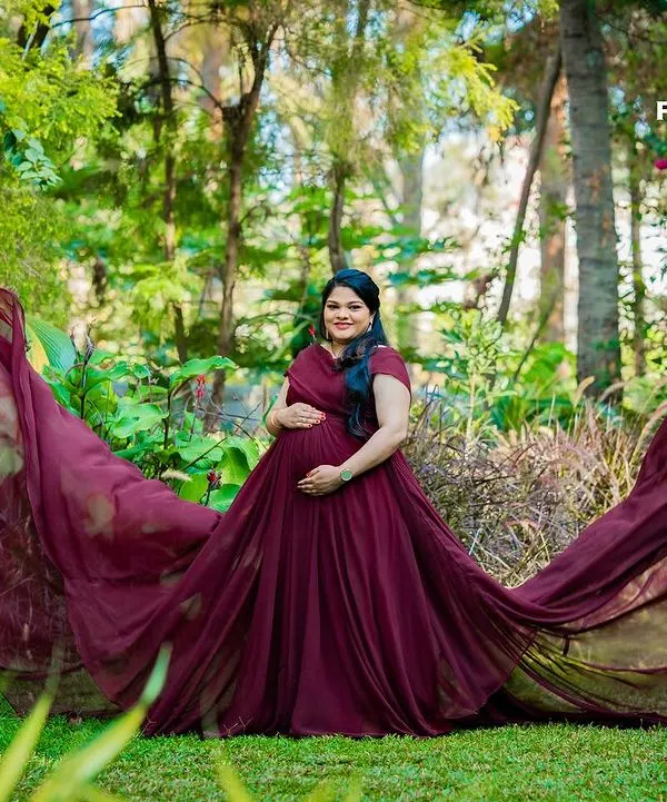 A cinematic solo maternity portrait in a lush garden setting, featuring a dramatic, flowing maroon gown that adds a touch of fairy-tale magic. This style is perfect for creating truly standout images.