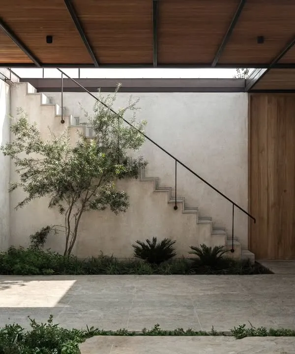 A central courtyard in a recently completed house, designed as a tranquil heart of the home. The inclusion of a tree and simple landscaping, combined with the concrete and wood material palette, creates a peaceful, private outdoor room.