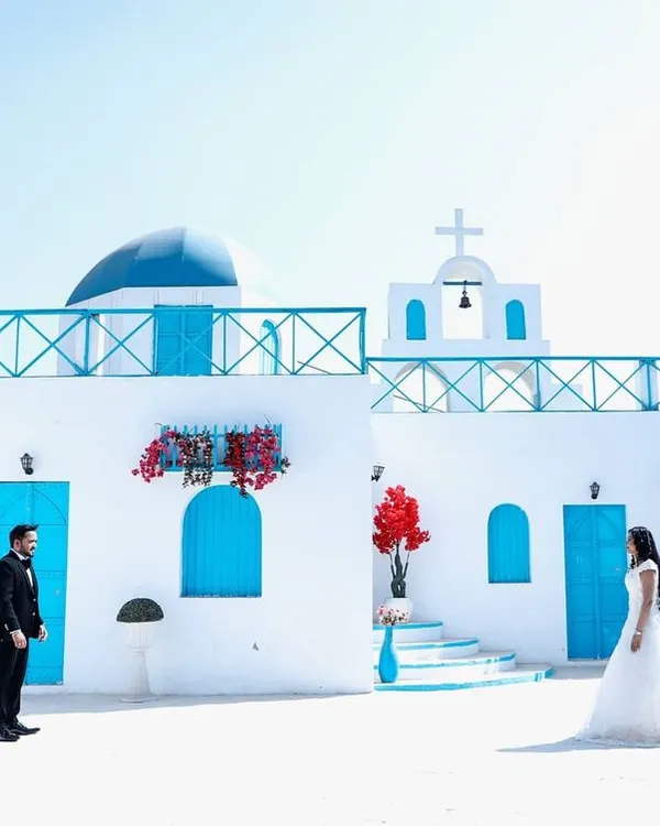 For this pre-wedding shoot, we used a stunning Santorini-style location to create a dreamy, romantic backdrop. This wide shot captures the beautiful architecture and the couple's elegant poses, perfect for a save-the-date announcement.