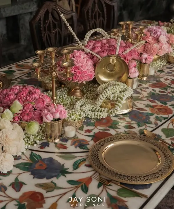 Dinner table settings that are anything but simple. For this wedding, I designed a tablescape on a stunning marble inlay table, featuring pink roses, jasmine garlands, and traditional brass plates for a refined and memorable dining experience.