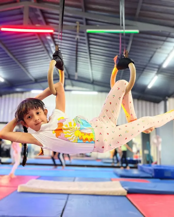 This is what pure joy in motion looks like. Here, one of our young gymnasts builds incredible upper body strength on the Roman rings, all while flashing a confident smile. We focus on making fitness fun and accessible.