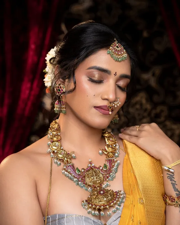 This look is inspired by the timeless paintings of Raja Ravi Varma. The antique necklace with a large central pendant, paired with matching jhumkas, vanki, and maang tikka, creates a truly artistic and classic bridal style.