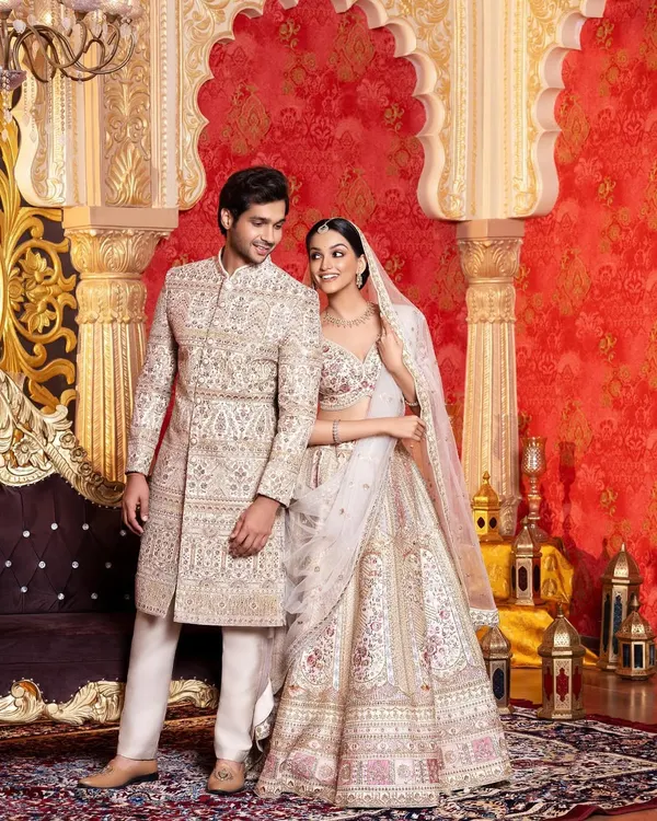 A stunning example of wedding day coordination. The bride and groom are dressed in matching ivory and gold outfits, with her lehenga and his sherwani featuring identical intricate embroidery, creating a seamless and royal look.